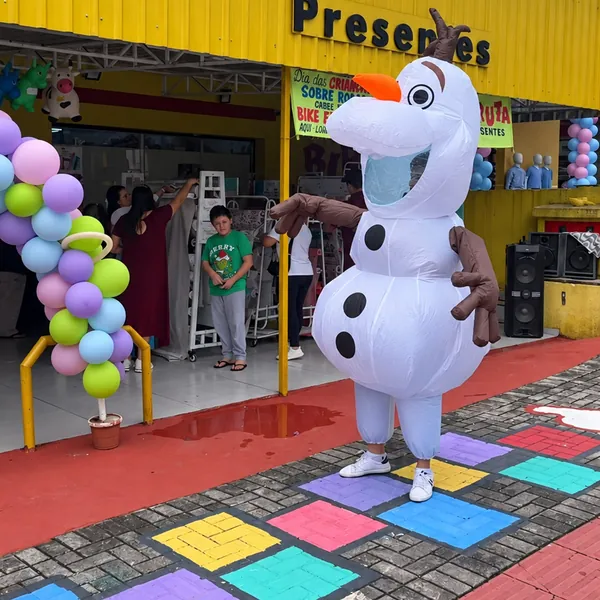 Personagem boneco de neve recebendo clientes na entrada da Biruta Presentes, com balões e amarelinha colorida